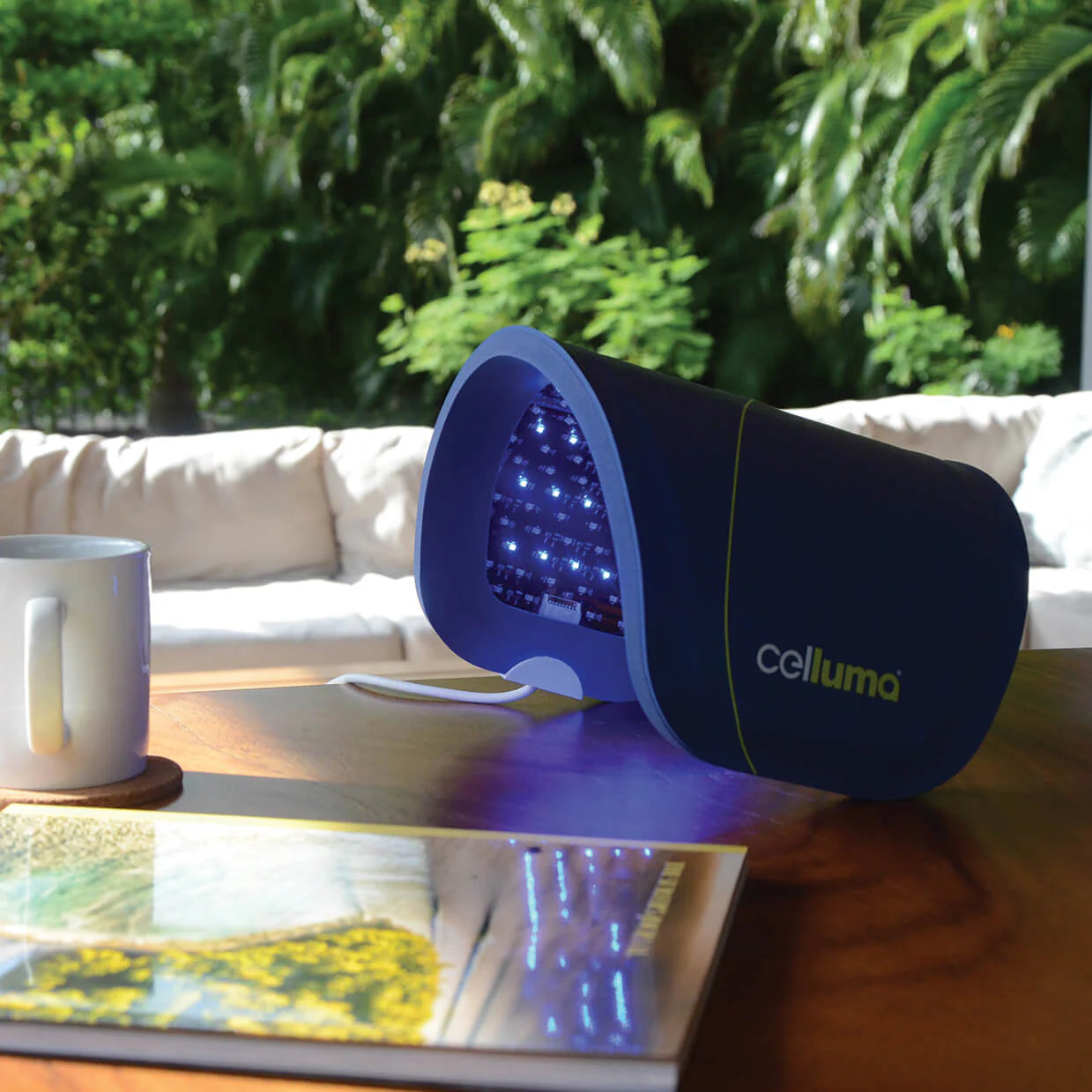 Celluma Lite Series 2 light therapy face mask on a table with a mug and book in a garden setting
